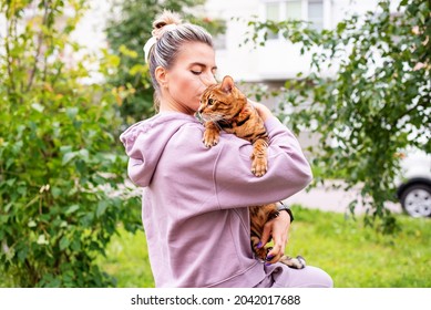 Young Woman Holding And Loving Her Bengal Cat Outside. Walk With Pet, Concept Of Pet Care, Cat On Harness, Daily Walking, Jogging, Training And Any Outdoor Recreations With Lovely Pet. 