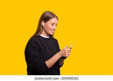 Young Woman Holding Mobile Cell Phone Listening To Music With Earpods Isolated On Yellow Background Studio