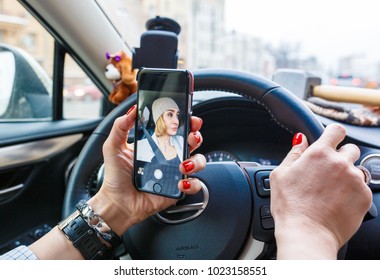 Young Woman Holding Mobile Phone And Taking Photos While Driving A Car. Smiling Girl Taking Selfie Picture With Smart Phone Camera Outdoors In Car