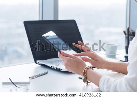 Young woman holding modern tablet computer, using device at workplace during break, chatting, blogging and posting information with apps.
