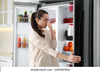 Young Woman Holding Nose Cause Of Bad Smell In Refrigerator In Kitchen