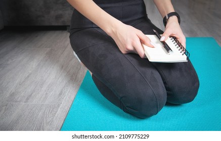 Young Woman Holding Notepad And Pen. Writes Training Plans At Home