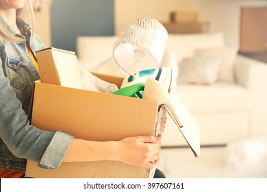 Young Woman Holding Open Cardboard Box With Things For Moving Into New House