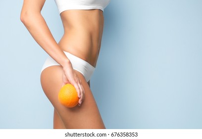 Young Woman Holding Orange On Light Background. Cellulite Problem Concept