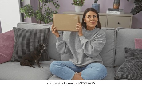 Young woman holding a package with a chihuahua beside her on a sofa at home - Powered by Shutterstock