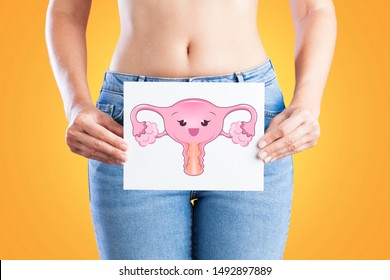 Young woman holding a paper with cartoon uterus drawing face on her waist. Hygiene, menses, fertility. Uterus health concept.