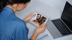 Young Woman Holding Photo Frame With Picture Near Laptop
