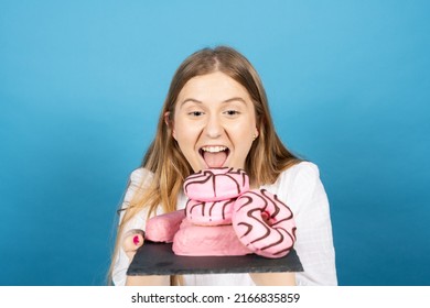 Young Woman Holding Pile Of Candy Sweet Food With Envy Isolated On Blue Background.. Bad Eating Habits Concept.