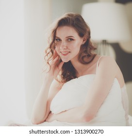 Young woman holding a pillow while sitting on her bed.