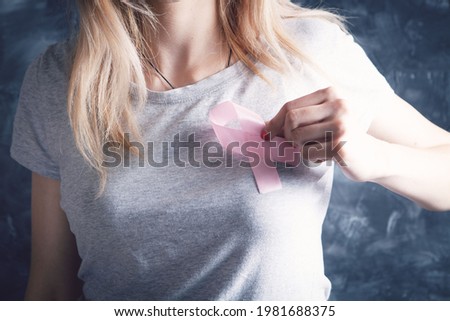 young woman holding pink ribbon near her chest on gray background