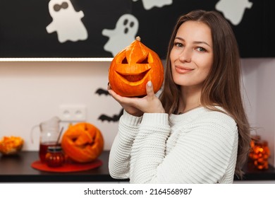 A young woman holding a pumpkin and getting ready for Halloween and looking into a camera