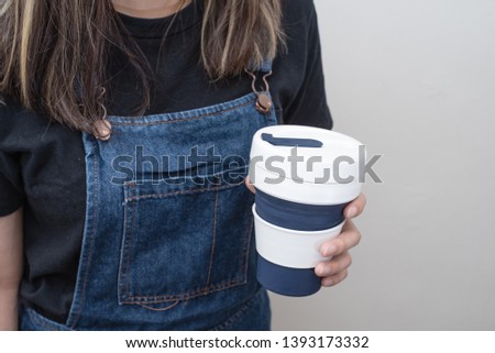 Young woman holding a silicone collapsible cup, reusable coffee tumbler.