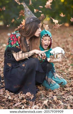 Young woman holding a skull, telling scary stories to a toddler boy in an autumn forest