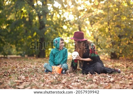 Young woman holding a skull, telling scary stories to a toddler boy in an autumn forest