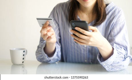 Young woman holding a smart phone and a card. Electronic payment concept.