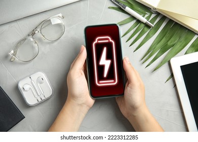 Young Woman Holding Smartphone With Low Battery At Grey Table, Top View