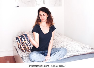 Young woman holding sneakers, sitting on a bed in a room, looking sad and bored, no motivation to do sport - Shutterstock ID 1855141897