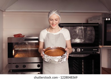 Young Woman Holding Sponge Cake Just From The Professional Oven On The Kitchen