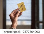 Young woman holding sticky paper note with sorry text and sad face emoticon over isolated background