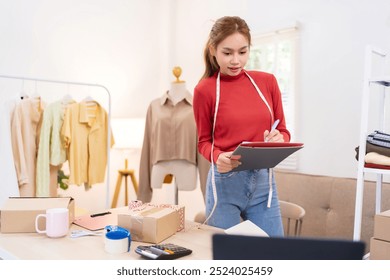 A young woman is holding a tablet and preparing to film content for her online clothing business. She is wearing a red sweater and working in an organized workspace - Powered by Shutterstock