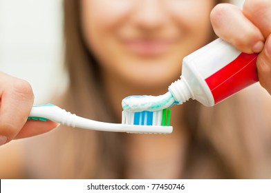Young woman holding a toothbrush and placing toothpaste on it.