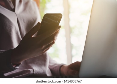young woman holding and using smart phone, touching screen and working on laptop - Shutterstock ID 1414803767