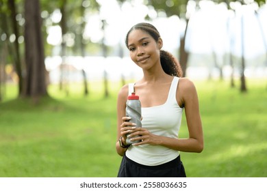 Young woman holding a water bottle while enjoying break during her outdoor exercise in a green park - Powered by Shutterstock