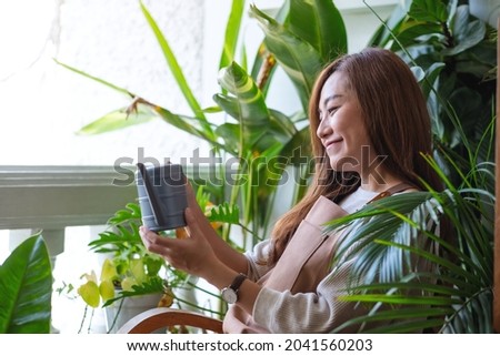 A young woman holding watering can while taking care and watering houseplants at home