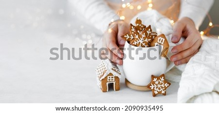 Young woman holding white mug with hot chocolate and gingerbread cookies. Holiday atmopshere, cozy handmade decor. Lights on background, bokeh. Close up copy space for text, banner