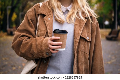 A young woman holds a craft disposable glass of coffee in her hand on a walk in the park, close up. - Powered by Shutterstock