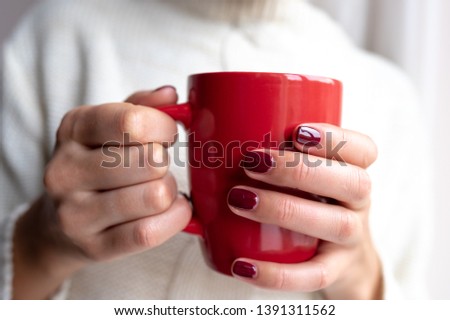 A young woman holds a cup with a hot drink in her hands.
