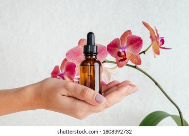 Young woman holds an essence for skin in her hands. Tropical orchid flowers. Unisex cosmetics. Place for  text.  Spa natural organic products.
Anti-age cosmetics for men and women. 