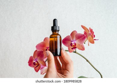 Young woman holds an essence for skin in her hands. Tropical orchid flowers. Unisex cosmetics. Place for  text.  Spa natural organic products.
Anti-age cosmetics for men and women. 