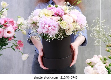 A young woman holds a flowerbox with peonies and roses. 