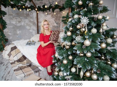 A young woman holds a gift near the Christmas tree. The girl smiles sitting with a gift for Christmas. Christmas tree upside down.
