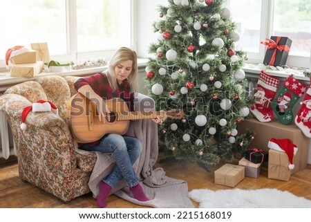 young woman holds a guitar in hand and sits in christmas studio