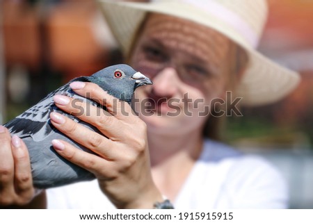 A young woman holds in the hands of a mail pigeon.  She is looking forward to his return from a long journey.