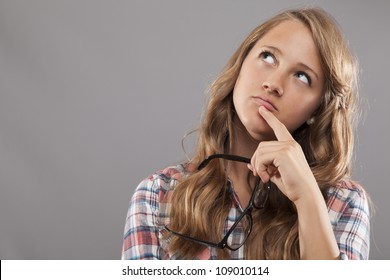 Eine junge Frau hält ihre Brille und schaut auf, während sie überlegt