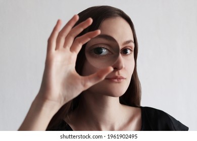A young woman holds a magnifying glass near her eye. Medical eyeglass lens visually enlarges a person eyes. Conceptual creative photo