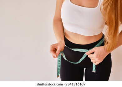 Young woman holds a measuring tape on her thin waist. Fitness instructor. The concept of nutrition, training and proper lifestyle. Beauty and weight loss