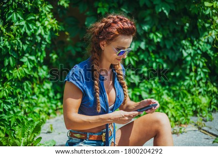  A young woman holds a mobile phone in her hands and presses a finger on the screen sensor.