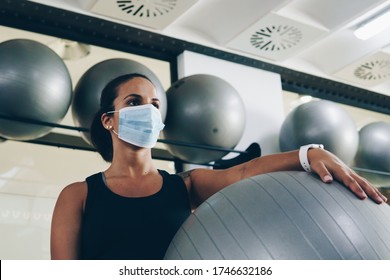 Young Woman Holds A Pilates Ball In The Gym. She's Wearing A Mask.