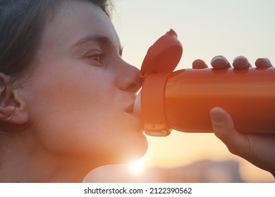 Young Woman Holds A Reusable Steel Stainless Water Bottle And Drinks Tea Or Water At Sunset Or Morning Sunlight