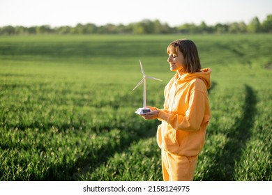 Young woman holds toy wind generator while standing on a green field on sunset. Concept of ecological and alternative energy