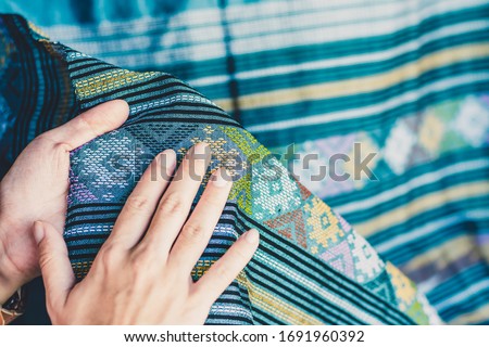 A young woman holds the traditional woven cloth and rubs her hand on the beautiful pattern of the woven fabric. The Thai folk weaving fabric.