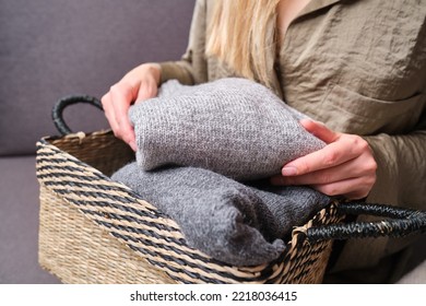 A Young Woman Holds Warm Knitted Sweaters And Puts Them In A Basket. Cozy Angoras Or Cashmere Things. Things After Washing
