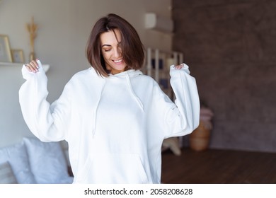 Young woman at home in the bedroom in a warm white hoodie, happy, posing, smiling, cozy winter evening