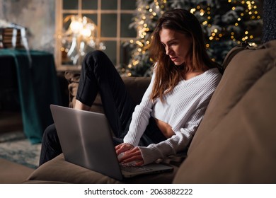 Young woman at home by Christmas tree sitting with laptop - Powered by Shutterstock