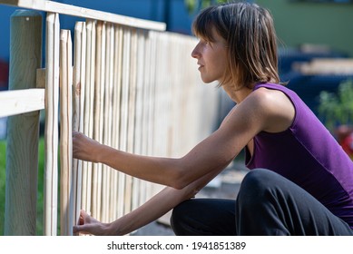 Young Woman In A Home Diy Project Making A Fence Of Wooden Planks Outside In Backyard.