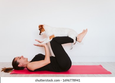 young woman at home doing yoga on a mat. cute small dog besides. healthy lifestyle concept